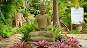 A section of Hunte’s Gardens at Bridgetown, Barbados with a Buddha statue surrounded by plants, foliage and a sign that reads ‘Hunte’s Gardens A Brief History’