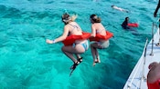 Dos Visitantes saltan al agua desde un catamarán mientras otros practican esnórquel en las cercanías