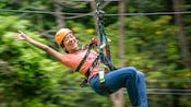 Person wearing a helmet and harness glides on a zip line through a lush forest canopy