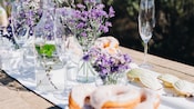 A picnic table with champagne glasses, pastries, madeleines and small bouquets of lavender