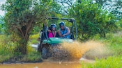 Guests driving a dune buggy through a puddle on a dirt trail