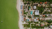 An aerial view of the beach retreat, with swimming pools, areas with lounge chairs and umbrellas, and surrounding greenery