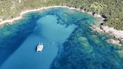 A catamaran sailing through Mediterranean waters off the shoreline of Ajaccio, Corsica, with swimmers nearby