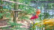 A woman zip lining near a river and a platform at Fun Forest climbing park