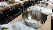Long tables lined with metal bowls filled with flour next to aprons that say ‘Mamo Pizza’