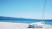 A small sailboat on a sandy beach near the ocean