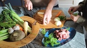 Two adults preparing vegetables on a cutting board in a kitchen