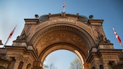 A monumental entrance arch with ornate carved stonework and Danish flags flanking the entrance of Tivoli Gardens in Copenhagen, Denmark