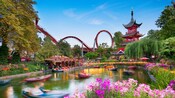 Tivoli Gardens featuring a roller coaster, Chinese pagoda tower, tranquil pond and vibrant flowers in Copenhagen, Denmark