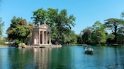 People in small paddleboats rowing through a serene lake near a classical temple near shore