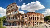 The curved outer wall of the Colosseum, with tourists walking to and from the gates