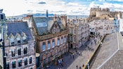 People on a street lined with historical buildings, with a plaza and Edinburg Castle at its end