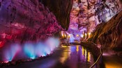 An underground cave passage with rock walls, a water channel and a pathway with a railing