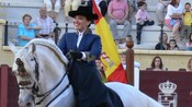 A woman in a formal hat and coat riding side saddle on a horse with a braided mane