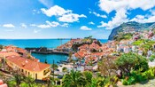 Un pueblo costero con edificios estrechamente agrupados detrás de escarpados acantilados y un puerto pequeño