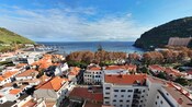 A coastal village with closely built structures, trees and a bay between 2 hills