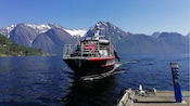 A touring boat with Guests seated on its deck approaching a dock on Hjorundfjord