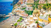 Dozens of buildings lining the hillside of the Amalfi Coast overlooking a small beach with boats
