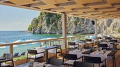The outdoor patio of the Riva Restaurant with a wooden ceiling and tables set for dining, overlooking a scenic rocky coastline