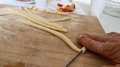 A person cutting pasta dough on a wooden surface