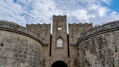 Una puerta medieval de piedra con paredes fortificadas, almenas y una entrada arqueada