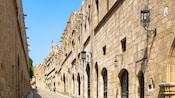 A cobblestone street lined with medieval stone buildings featuring arched doorways, lanterns and historic architecture