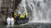Guests with their hands in the air as they cruise next to the bottom of a waterfall