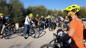 A group of cyclists wearing helmets gathered on a paved path surrounded by greenery