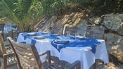 Mesa para comer en el exterior con mantel, camino y ubicaciones con platos, cubiertos y vasos