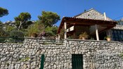 Stone villa with a terra cotta roof on a hillside with trees and potted flowers 