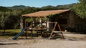 A playground with a slide and swings in front of stone building