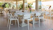 An open air restaurant with tables and chairs set for dining overlooking a beach