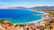 A crescent shaped bay in Rhodes with seaside buildings, small boats and mountains along the coastline