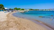 A beach in Rhodes featuring clear water, lounge chairs and beach umbrellas