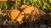 A wooden cart carrying large clay storage vessels surrounded by cactus plants in Rhodes, Greece