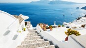 A stairway between traditional stone buildings descending toward the Santorini caldera