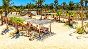 Palmeras y cabañas con camas de día, hamacas, mesas y toallas en un club de playa