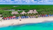 The shoreline of Kuza Beach, Mexico with rows of outdoor recliners and 3 large, thatched palapas