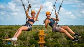 Two women gliding on a zip line over the lush jungle canopy of Cozumel