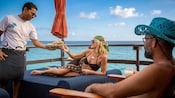 A server delivers food to a couple relaxing on a deck at BLU Floating Ocean Club