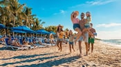 In Cozumel, Mexico, Disney Cruise Line Guests relax in lounge chairs in Disney’s exclusive beach zone at Kuza Beach while a family strolls along the shore