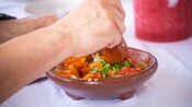 Hands grinding fresh tomatoes, peppers and cilantro in a clay bowl