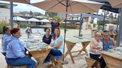 Visitantes sonriendo mientras están sentados en mesas de pícnic sombreadas con baldosas de cerámica pintadas