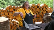 A woman holding a spatula over a grill during an outdoor cooking demonstration