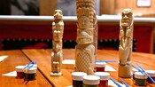 Unpainted mini totem poles, small containers of paint and paintbrushes on a table