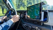 Two hands holding the steering wheel of a vehicle in motion alongside a GPS tablet