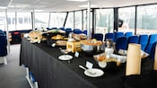 A buffet table setup with a variety of food inside a boat with rows of seats and large windows
