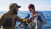 Two smiling men holding a cod fish on a fishing boat