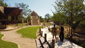 Two couples walking down a path at a garden featuring a thatched roof structure and a Mayan pyramid replica