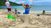 A Guest sitting with her legs inside of a mermaid tail sculpted out of sand
